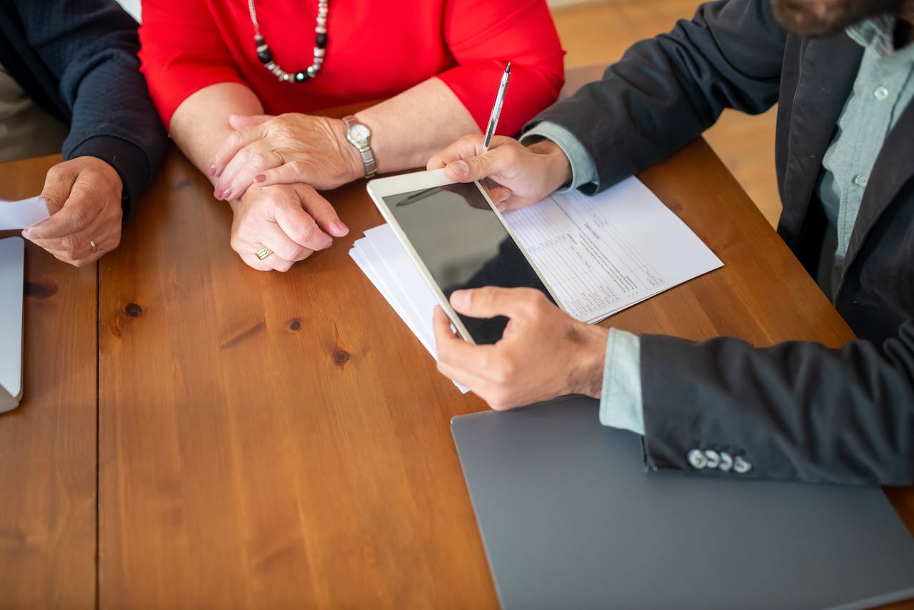 Home Business meeting at a wooden table with consultant reviewing documents and using a digital tablet.